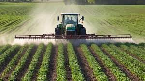 Green tractor with sprayer boom applying MaxxGro bulk agrochemicals over rows of crops, signifying efficient, large-scale application and reliable supply in the Indian market.