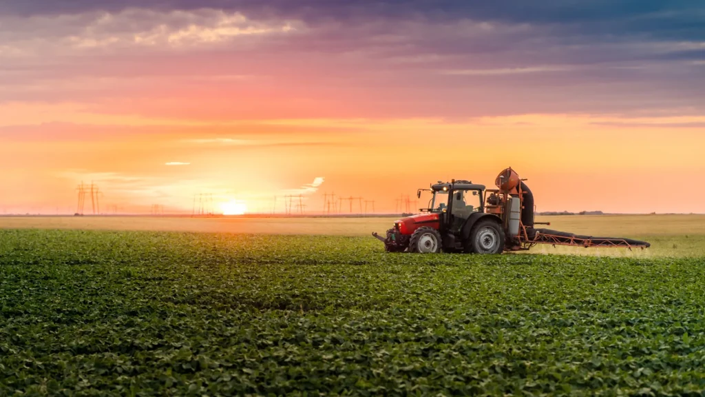 Tractor spraying high-efficiency crop protection insecticide over a green crop field at sunset.