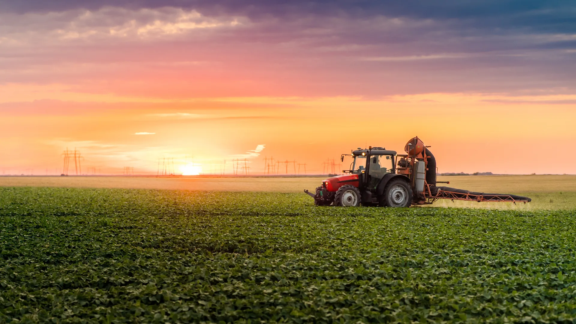 Tractor spraying high-efficiency crop protection insecticide over a green crop field at sunset.