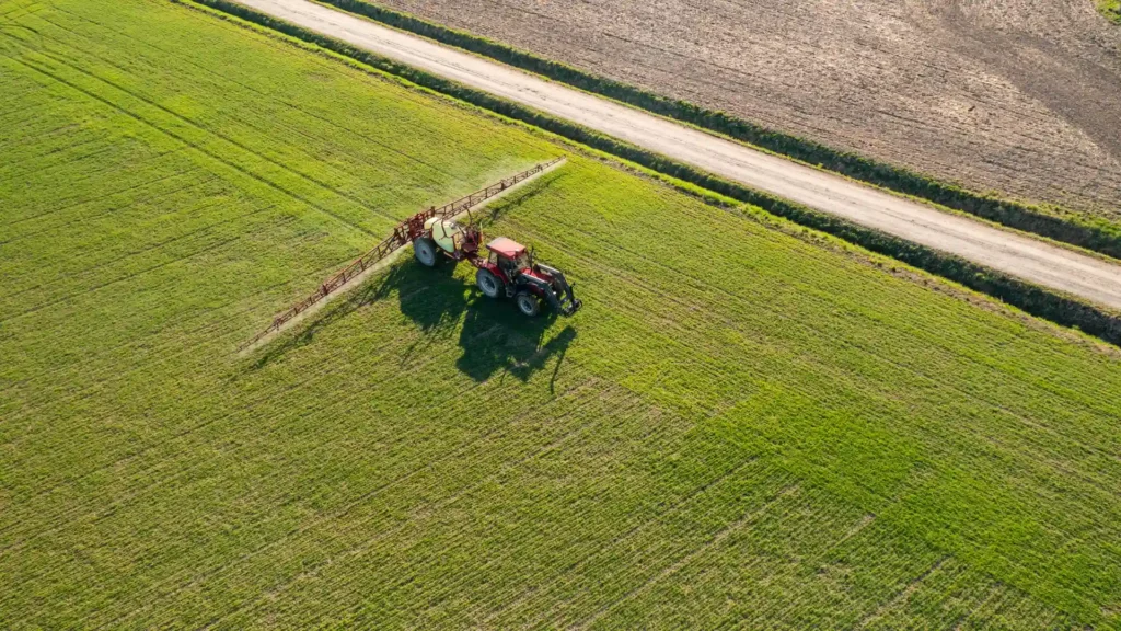 Aerial view of a tractor applying high-performance agrochemical crop spray across a lush green agricultural field.