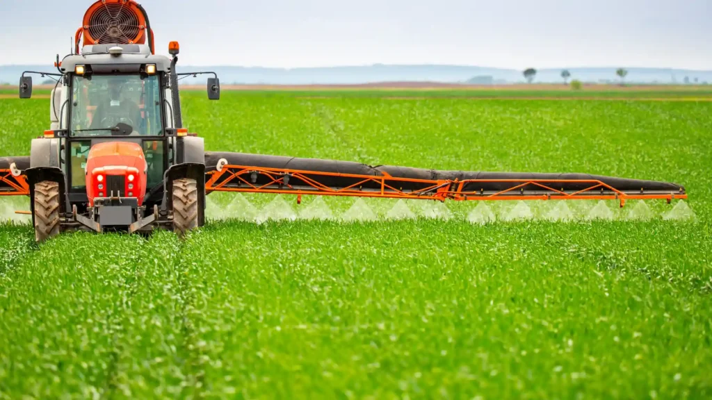 Modern agricultural tractor with a wide boom sprayer precisely applying agrochemical crop protection across a vibrant green field.