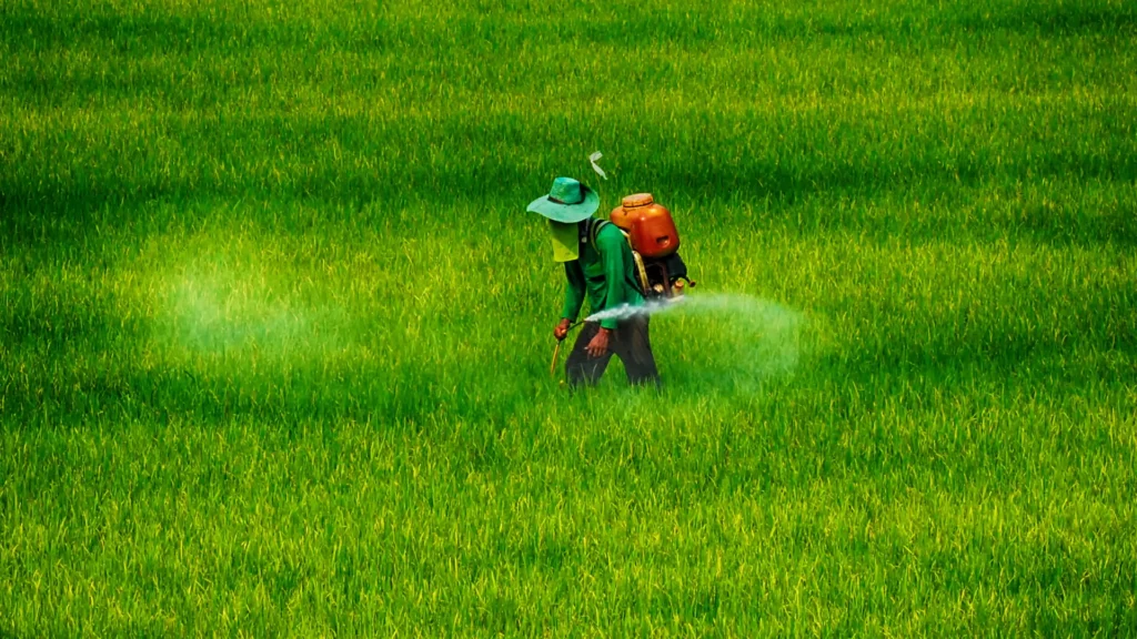 Farmer spraying crops in a lush green field with Deep Soil Agrology Limited agrochemical products like Azomaxx and Blaire in the foreground.